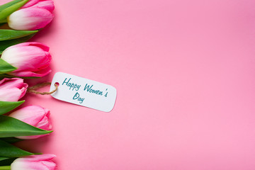 Top view of happy womens day lettering on paper label with row of tulips on pink background