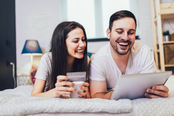 Happy couple shopping online at the comfort of their bedroom.