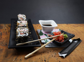 close view sushi on black rectangual plate with wasabi, ginger and soy in white bowl