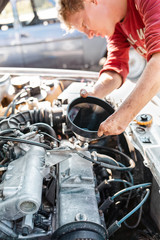 The concept of disability of people and their adaptation to life. A disabled blonde man repairs a car, pouring engine oil. There are no fingers on his hands. Disabled from childhood. Vertical