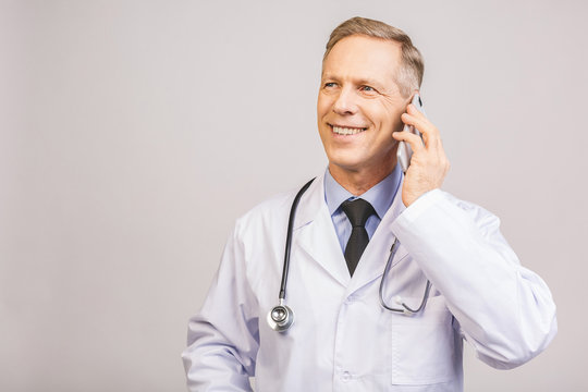 Closeup photo of senior man doctor standing isolated on grey background, using mobile phone.