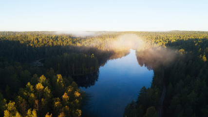 Early misty morning, sunrise over lake. Beautiful forest and sun rays. Aerial view. Finland, Nuuksio. 