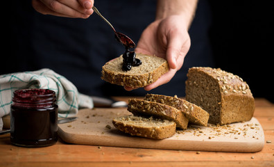 Person applying jam to fresh bread, visible moment of the jam flowing onto a slice of bread, dark...