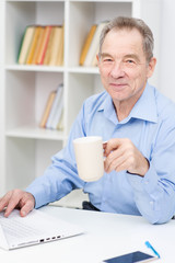 Portrait of modern senior man using laptop at home working and filling in papers