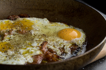 Close up of a fried egg with bacon lying in a pan, strong bacon cooking, warm kitchen light
