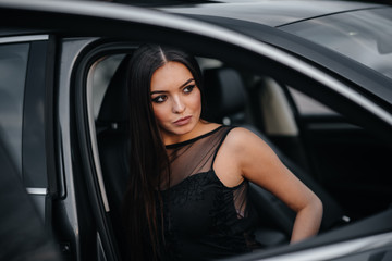Plakat Stylish young girl sitting in a business class car in a black dress. Business fashion and style