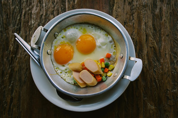 top view thai food Fried egg on the pan With chicken sausage, corn, carrots, nuts on wooden table