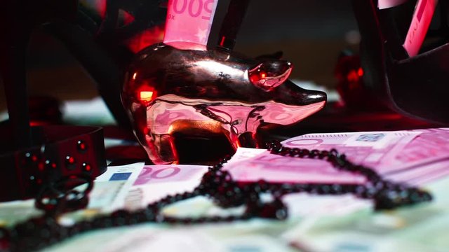 Golden pig piggy bank stands under high heels of women's shoes. Nearby are euro bills and a collar with a chain. BDSM practice concept.