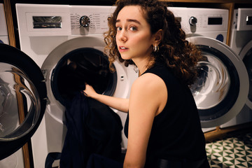 Pensive brunette girl washing clothes in self-service laundry
