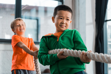 Selective focus of multicultural children playing tug of war in gym