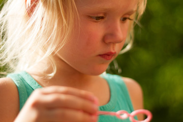 Pretty blond toddler girl wearing cat's headband making bubbles on a sunny summer day