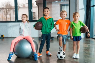 Zelfklevend Fotobehang Front view of Child sitting on fitness ball next to multiethnic children with balls in gym © LIGHTFIELD STUDIOS