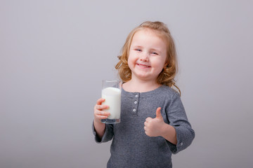 Little happy girl child smiling with a glass of milk, shows class. isolated on a gray background Is the concept of baby food
