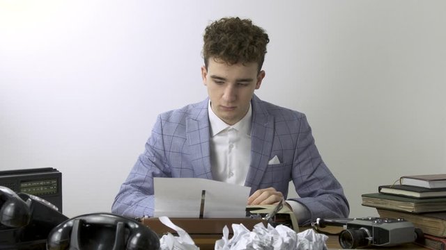 Retro 80s  young man Writer thinks over text of book or a script and typing on typewriter. unsuccessful attempt concept.