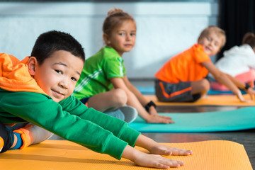 Selective focus of multicultural children with crossed legs stretching on fitness mats