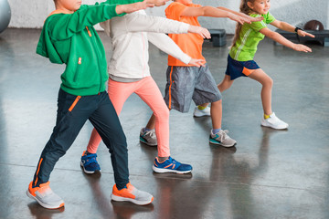 Cropped view of children with outstretched hands doing lunges in gym