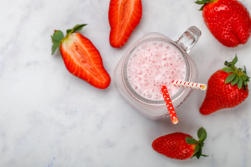 smoothie or milkshake of fresh strawberries, yogurt or milk and ice cubes in Mason jar on a marble table. Concept of healthy vitamin drinks. Selective focus, top view, copy space