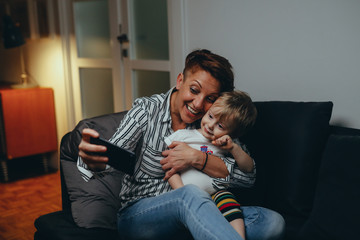 mid aged woman with her son relaxed on sofa using mobile phone at her home