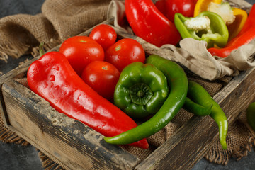 Green and red chilies with tomatoes in a wooden tray.