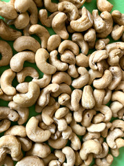 Food background. Cashew kernels close-up. A pile of large nuts on a green background. The texture of nuts. Close-up, vertical, top view. Healthy eating concept.