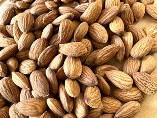 Food background. Many peeled almonds on a wooden background. Texture of almond kernels. Background of brown nuts. Close-up, horizontal, cropped shot. Concept of vegetarianism and healthy eating.