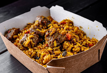 Rice with meat and vegetables in a box on on dark wooden table background