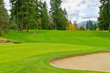 Golf course with gorgeous green, sand bunker and golf flag.