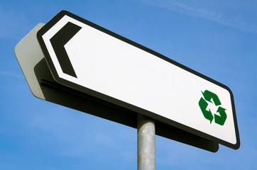 Blank sign with copy space next to recycling symbol standing in bright blue sky