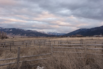 Fototapeta na wymiar Vintage western wood slate fencing in an overgrown pasture with snow capped mountain range in the distance