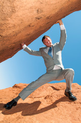 Strong office worker straining to lift massive rock outdoors 