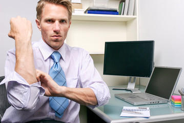 Serious businessman rolling up his sleeves to get down to work in his office cubicle