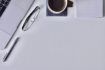 Worktable with laptop, glasses, pen, block and mug of black coffee