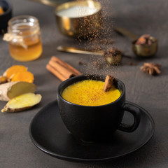 Cinnamon pouring on dark mug with Golden milk drink. Tasty Ayurvedic beverage for cold day.