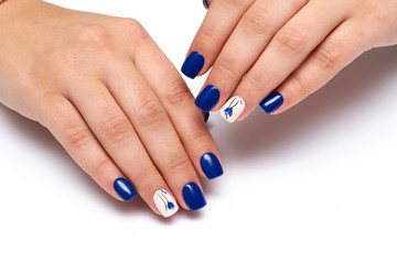Blue manicure with a beige ringless nail and painted flowers on short square nails. Gel coating of nails. Close-up.