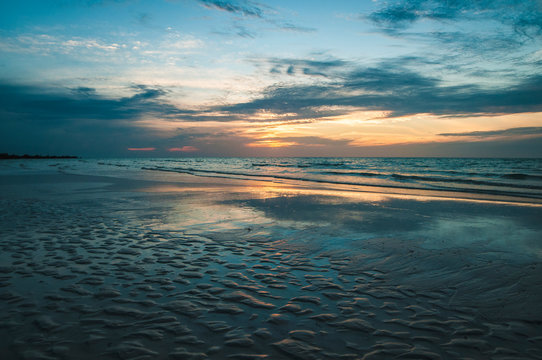 Calm tranquil seascape of empty beach and wavy ocean under blue cloudy sky with orange sunlight in gloomy d ay