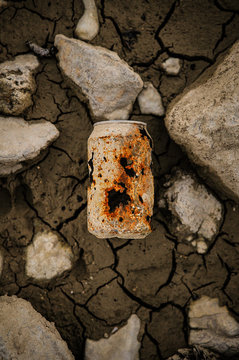 From above rusty shabby old can on cracked dark terrain with stone