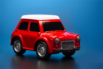 Red colored little toy model car on a blue background.