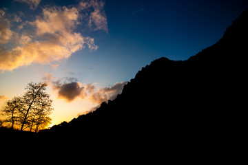 Sunset with clouds and silhouettes of trees and hills