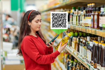 A young Caucasian woman scans the qr code on an oil bottle using her smartphone. Qr code icon above...