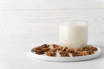 Walnut milk in a glass cup and nuts on a flat plate, white background. Dairy products without lactose. Horizontal orientation with copy space.