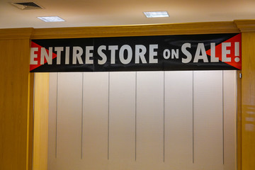 A sign that says entire store on sale hanging from the ceiling above a blank empty wall