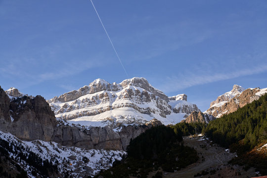 Stony snowy rocks and sloppy valley with evergreen forest in bright day
