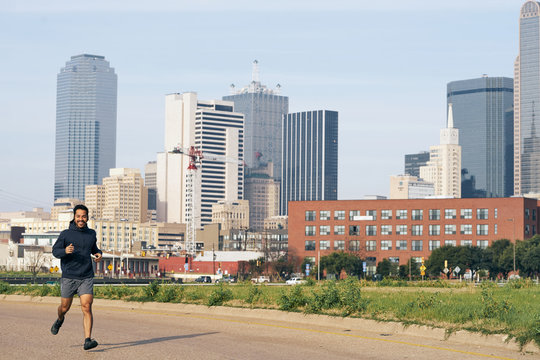 Overjoyed Hispanic male runner in active wear laughing and looking at camera with powerful downtown on background 