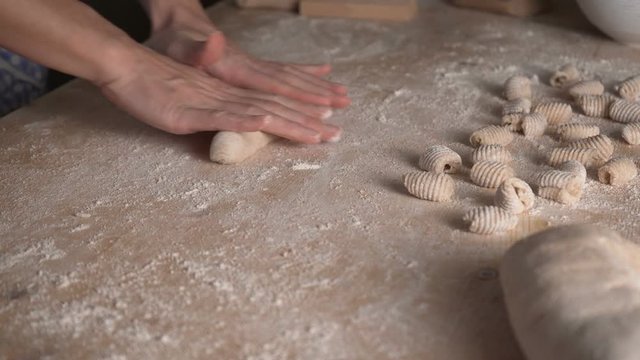 Close up process of homemade vegan gnocchi pasta with wholemeal flour making. The home cook rolls the dough on the wooden chopping board , traditional Italian pasta, woman cooks food in the kitchen