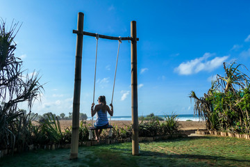 A girl swinging on a bamboo swing with the view on Nyang Nyang Beach, Bali, Indonesia. The swing has very simple construction. Hidden getaway. Collecting happy moments and having fun.