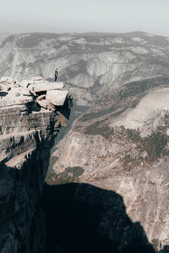 Young woman standing ontop of Half Dome looking over a cliff