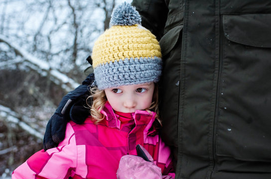 young girl looking sad cuddling her dad whilst playing outside in snow