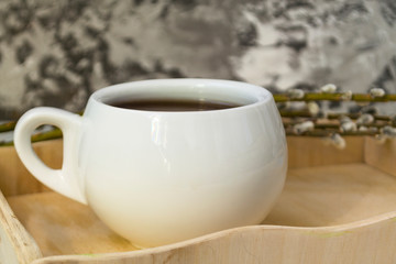 A willow twig with buds and a white cup of tea stands on a wooden tray. The concept of morning, breakfast