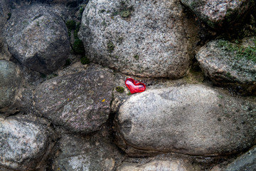 Red glass heart among the stones. Background.