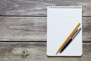 Notepad with a blank white sheet in a checker paper with ball pen and simple graphite pencil lies on the background of wooden boards